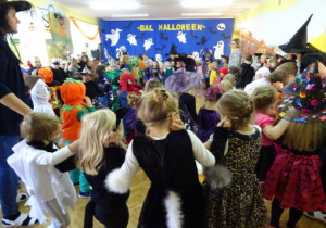Wszystkie dzieci tańczą w kole, w tle dekoracja halloweenowa.